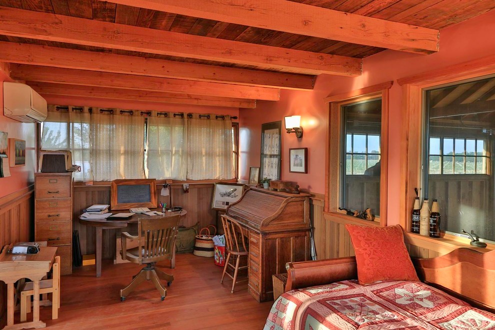 Foto på ett lantligt arbetsrum, med orange väggar, mellanmörkt trägolv och ett fristående skrivbord
