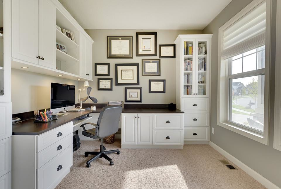 Modelo de despacho de estilo americano de tamaño medio sin chimenea con paredes beige, moqueta y escritorio empotrado
