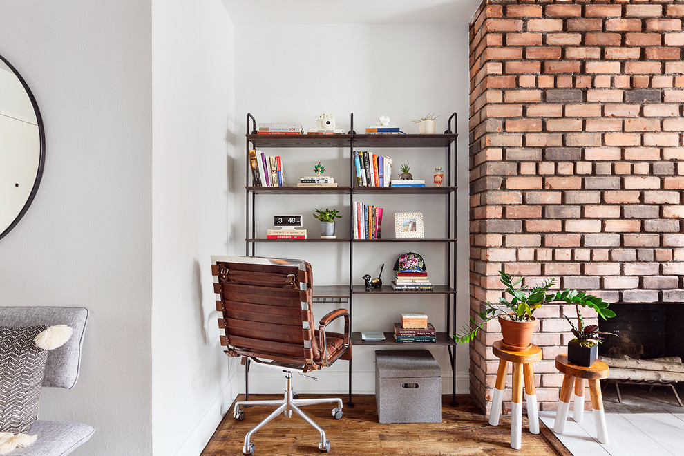 Cette image montre un petit bureau vintage avec un mur blanc, un sol en bois brun, une cheminée standard, un manteau de cheminée en brique et un bureau indépendant.