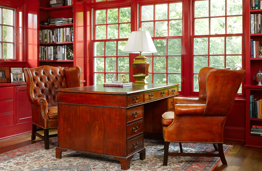 Foto på ett vintage hemmabibliotek, med röda väggar, mörkt trägolv och ett fristående skrivbord