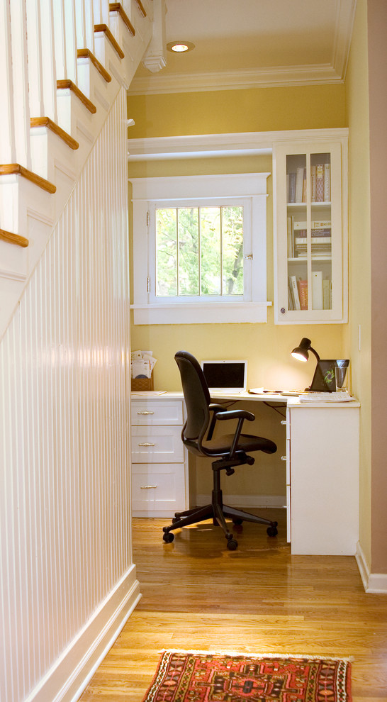 Imagen de despacho de estilo americano pequeño sin chimenea con paredes amarillas, suelo de madera clara y escritorio empotrado