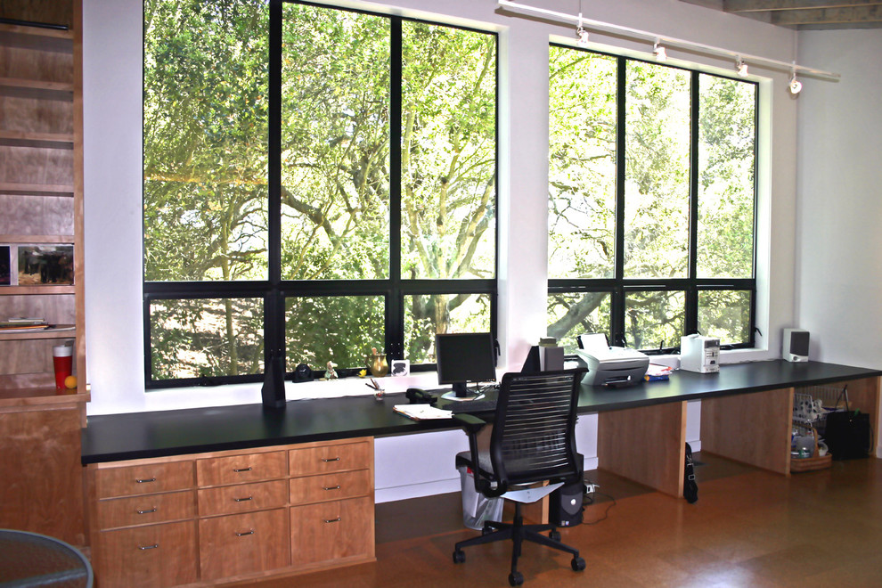 Immagine di un piccolo atelier moderno con pareti bianche, pavimento in sughero e scrivania incassata