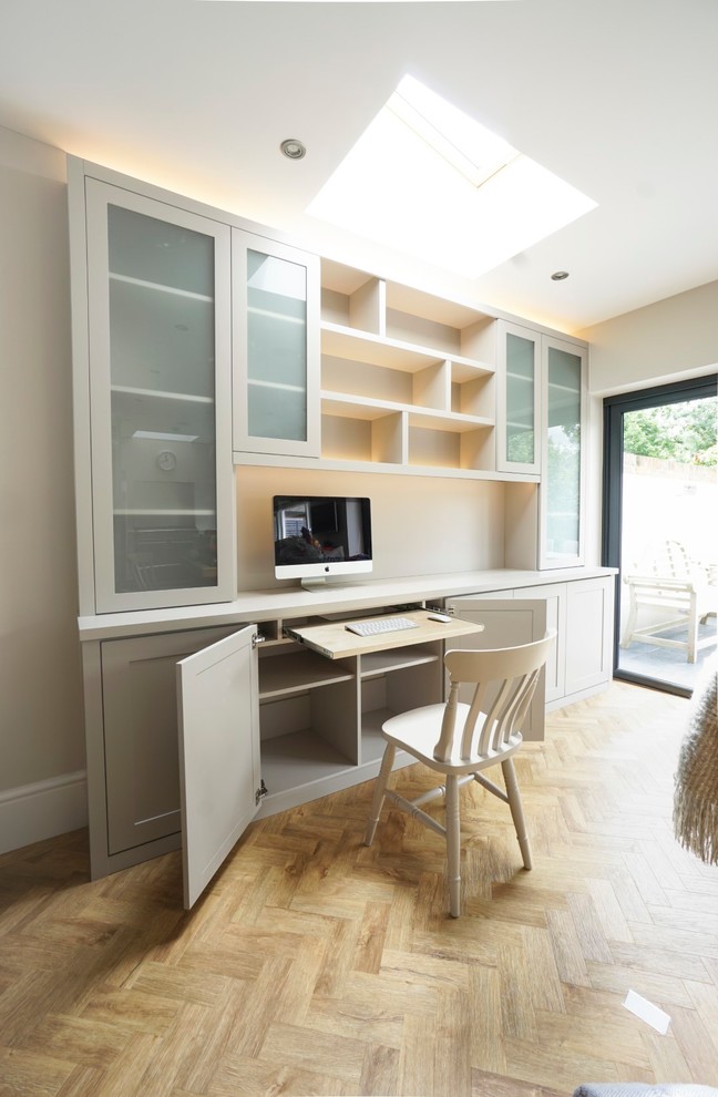 This is an example of a small contemporary study in Buckinghamshire with beige walls, light hardwood flooring, a built-in desk and beige floors.
