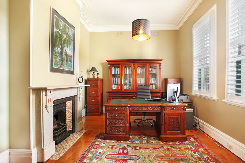 Modelo de despacho tradicional pequeño con paredes amarillas, suelo de madera clara, todas las chimeneas, marco de chimenea de piedra y escritorio independiente