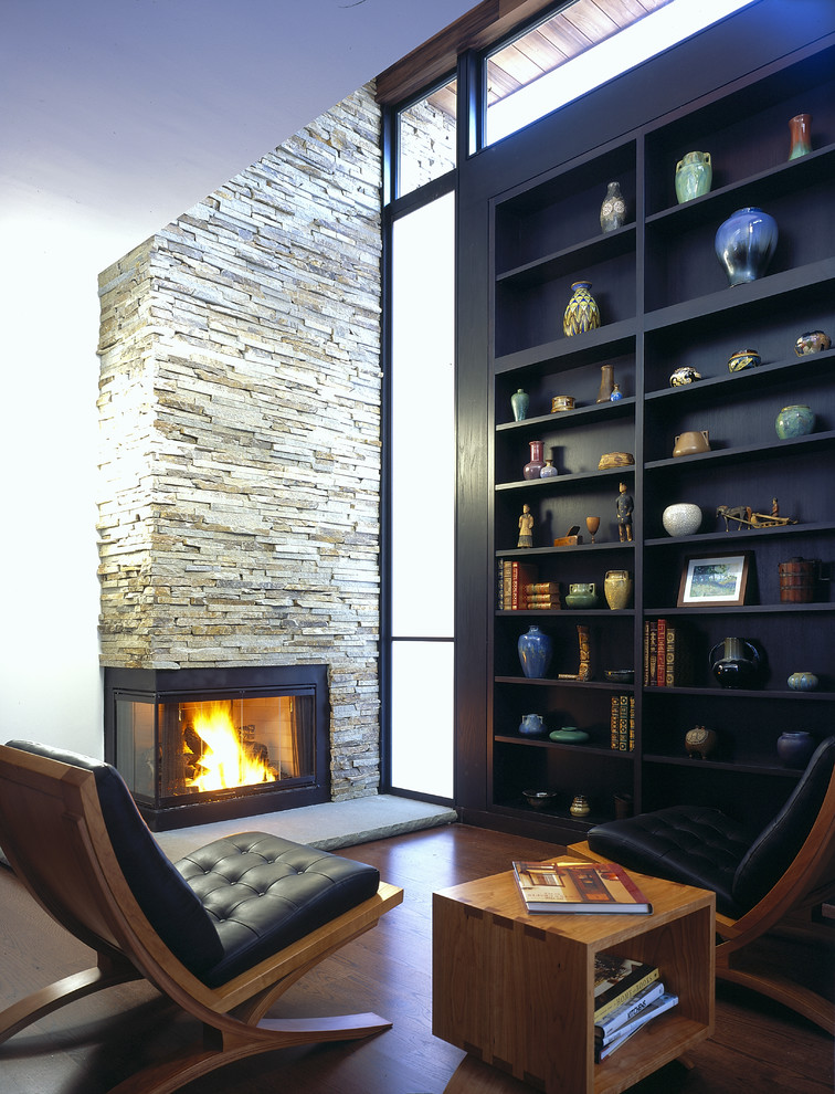 Cette image montre un bureau design avec une bibliothèque ou un coin lecture, parquet foncé, une cheminée d'angle et un manteau de cheminée en pierre.