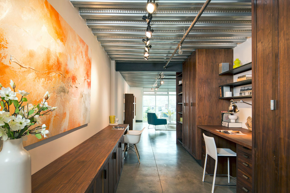 Diseño de despacho urbano de tamaño medio sin chimenea con paredes blancas, suelo de cemento y escritorio empotrado