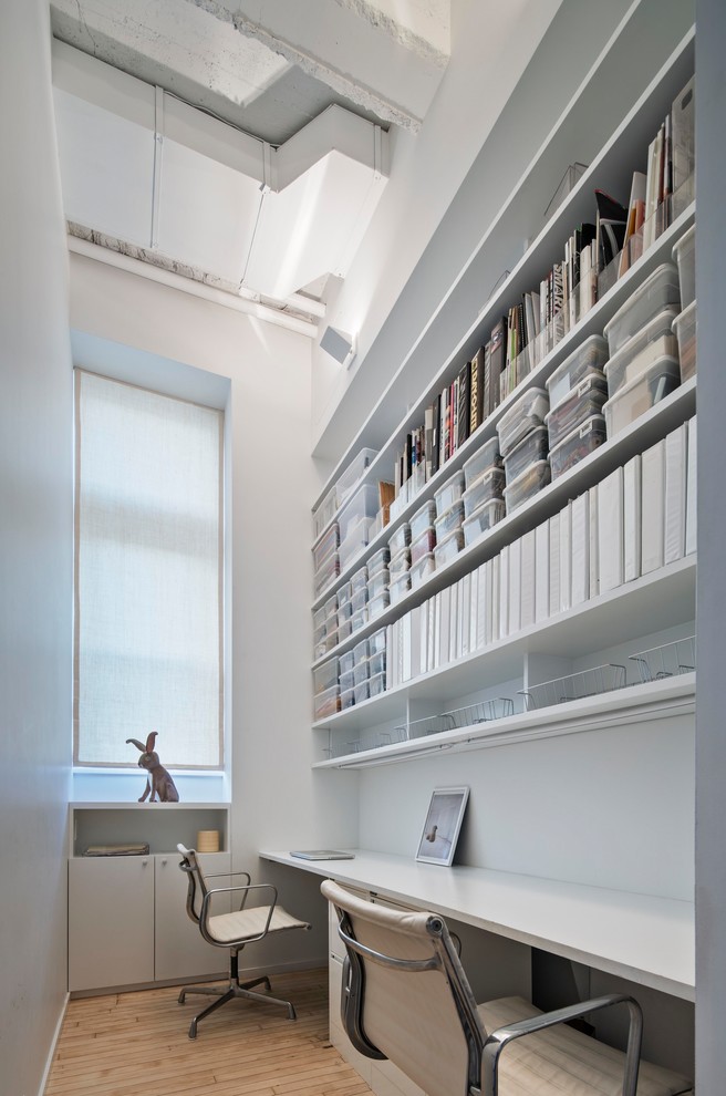 Inredning av ett modernt litet hemmabibliotek, med vita väggar, ljust trägolv, ett inbyggt skrivbord och beiget golv