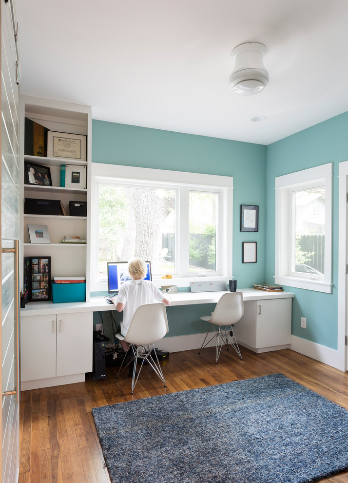 Inspiration för små klassiska hemmabibliotek, med ett inbyggt skrivbord, blå väggar, mellanmörkt trägolv och brunt golv
