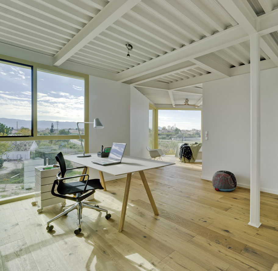 Ejemplo de despacho industrial de tamaño medio sin chimenea con paredes blancas, suelo de madera en tonos medios y escritorio independiente