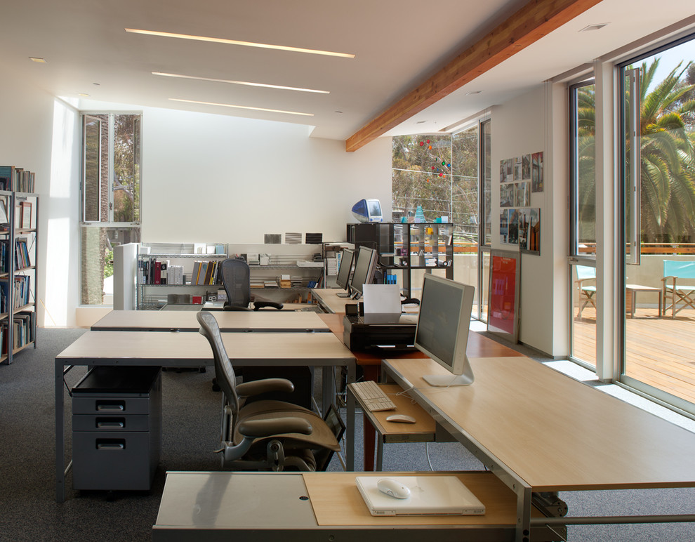 Modern inredning av ett arbetsrum, med vita väggar, heltäckningsmatta och ett fristående skrivbord