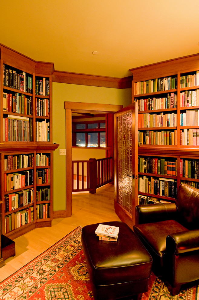 Amerikansk inredning av ett mellanstort hemmabibliotek, med beige väggar och ljust trägolv