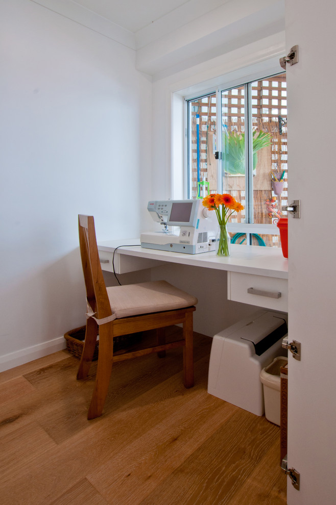 Exemple d'un petit bureau atelier moderne avec un mur blanc, un sol en bois brun, aucune cheminée et un bureau intégré.