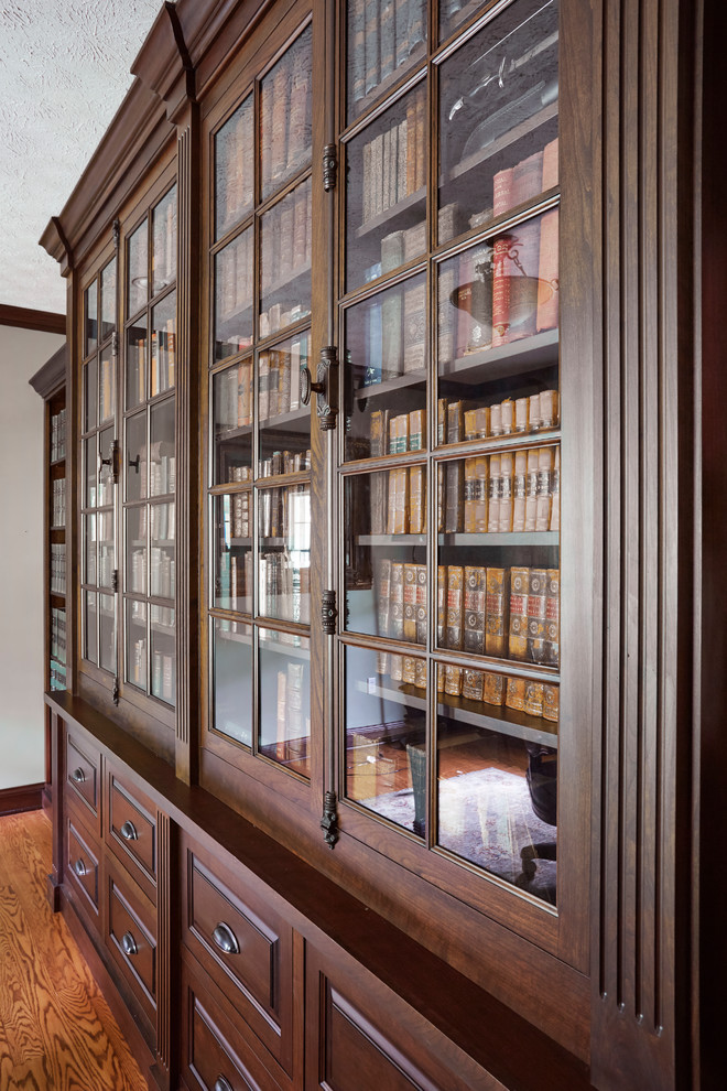 Cette image montre un bureau traditionnel avec une bibliothèque ou un coin lecture, un bureau intégré, un mur blanc, un sol en bois brun et un sol marron.