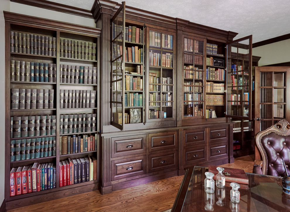 Klassisk inredning av ett arbetsrum, med ett bibliotek, ett inbyggt skrivbord, vita väggar, mellanmörkt trägolv och brunt golv
