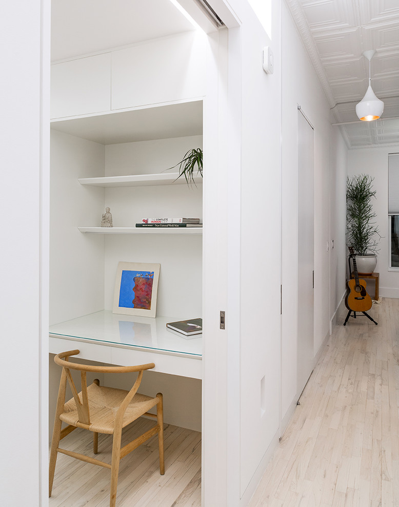 Nordisk inredning av ett litet arbetsrum, med vita väggar, ljust trägolv och ett inbyggt skrivbord