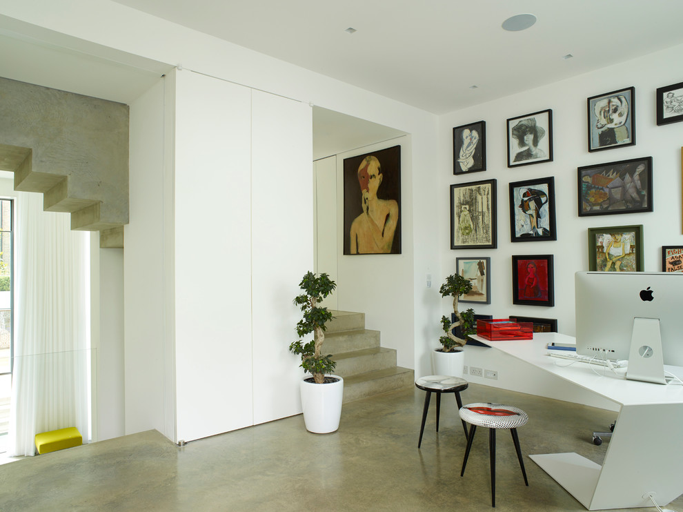 Стильный дизайн: большой кабинет в современном стиле с белыми стенами, бетонным полом, отдельно стоящим рабочим столом и серым полом - последний тренд