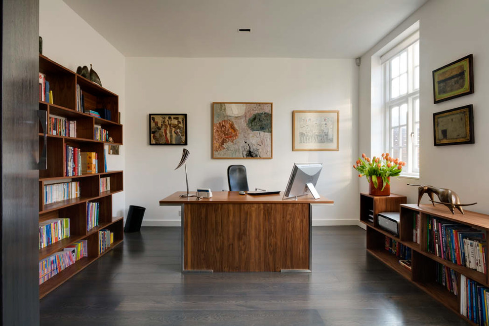 Großes Modernes Arbeitszimmer mit weißer Wandfarbe, dunklem Holzboden, freistehendem Schreibtisch und braunem Boden in London