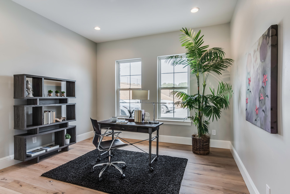 Modelo de despacho contemporáneo de tamaño medio sin chimenea con paredes grises, suelo de madera clara, escritorio independiente y suelo beige