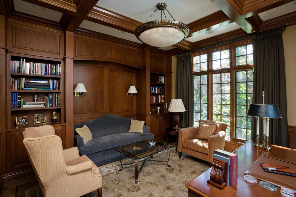 Diseño de despacho tradicional de tamaño medio con biblioteca, paredes beige, suelo de madera en tonos medios, escritorio independiente y suelo marrón