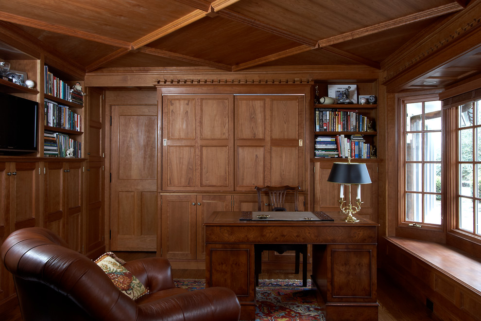 Foto på ett litet vintage arbetsrum, med ett bibliotek, bruna väggar, mörkt trägolv, en öppen hörnspis, en spiselkrans i sten, ett fristående skrivbord och brunt golv