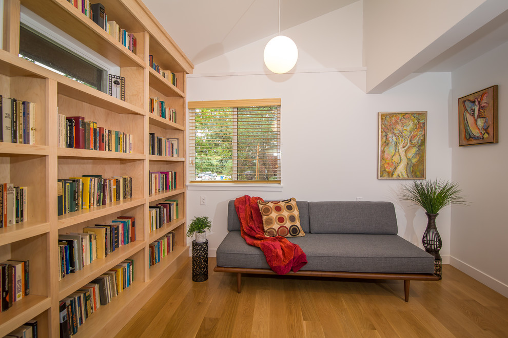 Foto på ett mellanstort 50 tals arbetsrum, med ett bibliotek, vita väggar och ljust trägolv