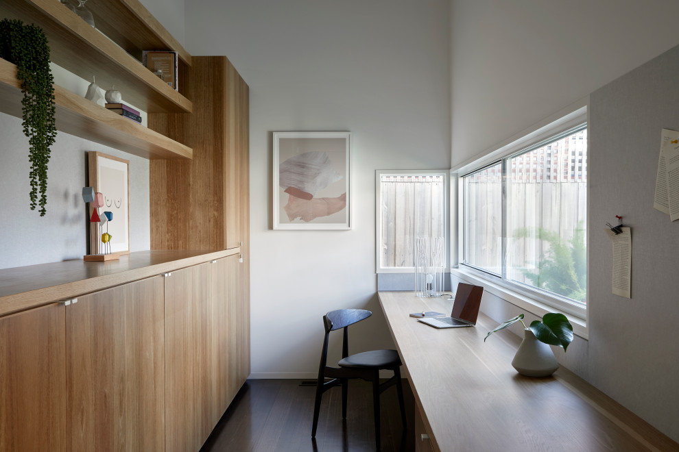 Großes Modernes Arbeitszimmer mit Arbeitsplatz, weißer Wandfarbe, dunklem Holzboden, Einbau-Schreibtisch und braunem Boden in Melbourne