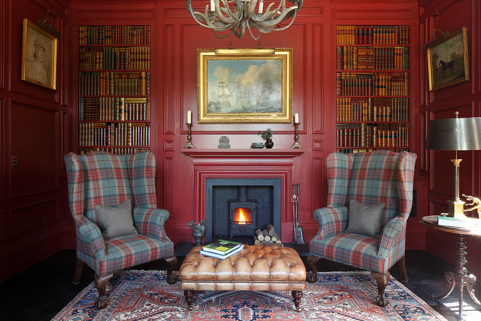 Aménagement d'un bureau romantique avec un mur rouge, parquet foncé, un poêle à bois et un manteau de cheminée en plâtre.