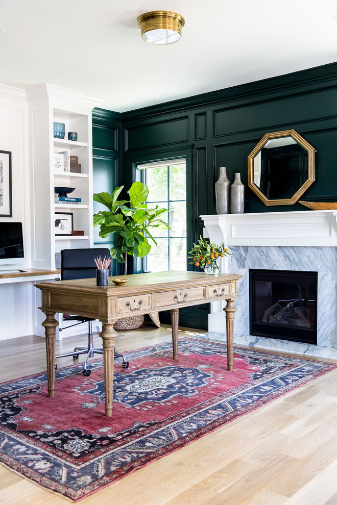 Imagen de despacho tradicional con paredes verdes, suelo de madera clara, todas las chimeneas, marco de chimenea de piedra y escritorio independiente