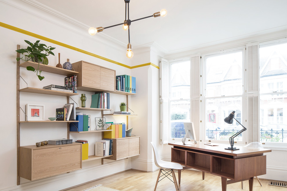 Foto på ett mellanstort minimalistiskt hemmabibliotek, med vita väggar, ljust trägolv och ett fristående skrivbord