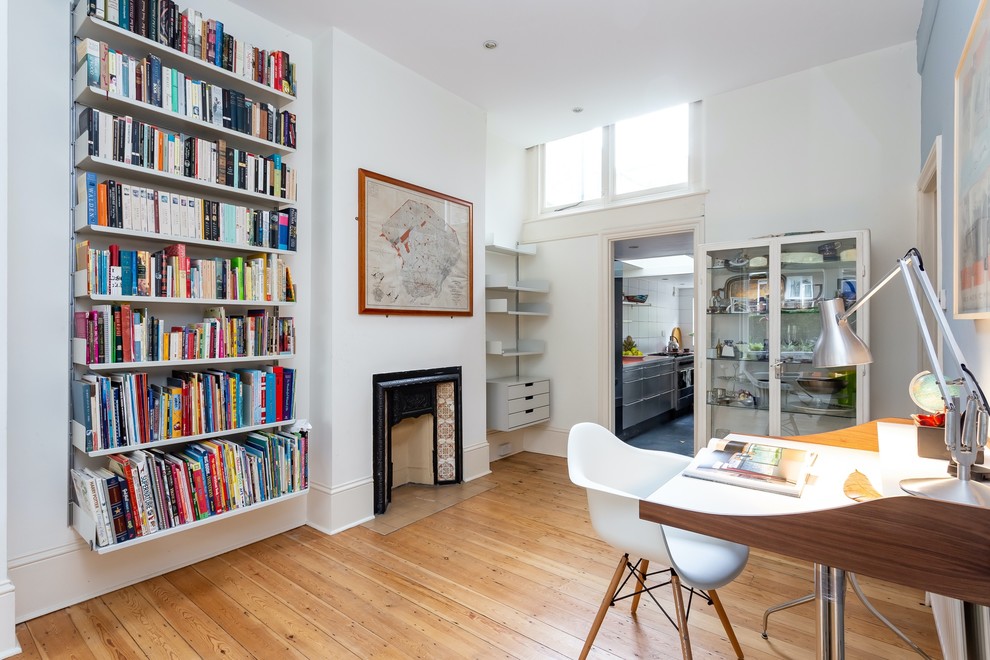 Foto di uno studio minimalista con pareti bianche, pavimento in legno massello medio, camino bifacciale, scrivania autoportante e pavimento marrone