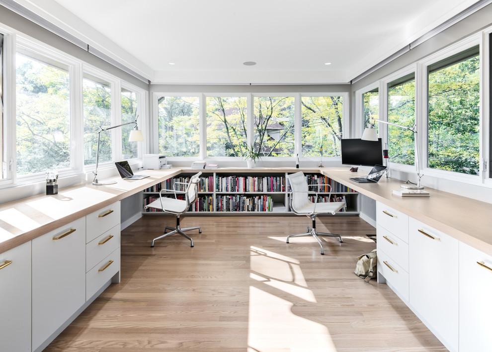 Bild på ett funkis arbetsrum, med ett bibliotek, ljust trägolv, ett inbyggt skrivbord och beiget golv