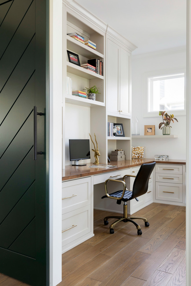 Imagen de estudio costero de tamaño medio con paredes blancas, suelo de madera en tonos medios, escritorio empotrado y suelo beige
