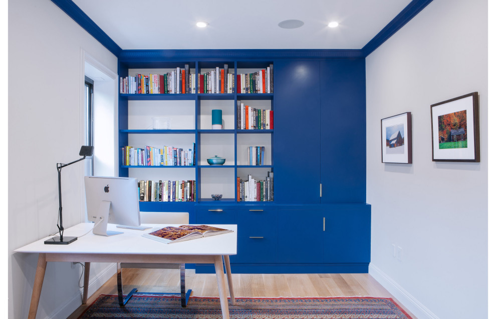 Modernes Arbeitszimmer ohne Kamin mit Arbeitsplatz, weißer Wandfarbe, braunem Holzboden, freistehendem Schreibtisch und braunem Boden in New York