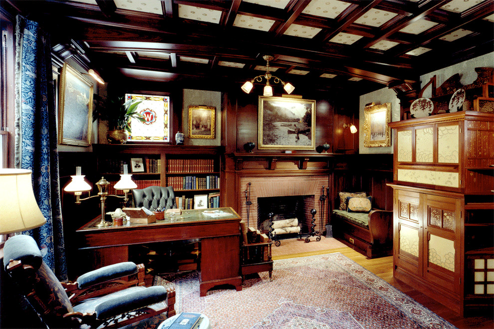 Inredning av ett klassiskt stort hemmabibliotek, med gröna väggar, mellanmörkt trägolv, en standard öppen spis, ett fristående skrivbord och en spiselkrans i tegelsten
