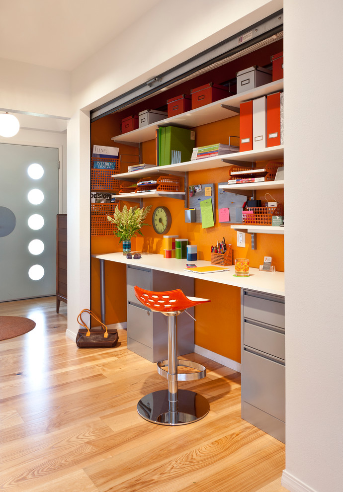 Cette photo montre un bureau rétro avec un mur orange, un sol en bois brun et un bureau intégré.