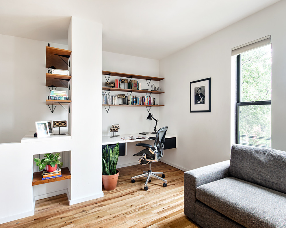 Exempel på ett litet minimalistiskt hemmabibliotek, med vita väggar, ljust trägolv och ett inbyggt skrivbord