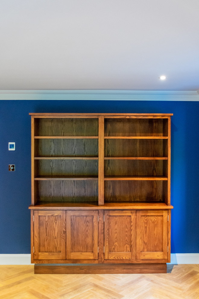 Exempel på ett stort klassiskt hemmabibliotek, med blå väggar, ljust trägolv, en öppen vedspis, en spiselkrans i tegelsten och ett fristående skrivbord