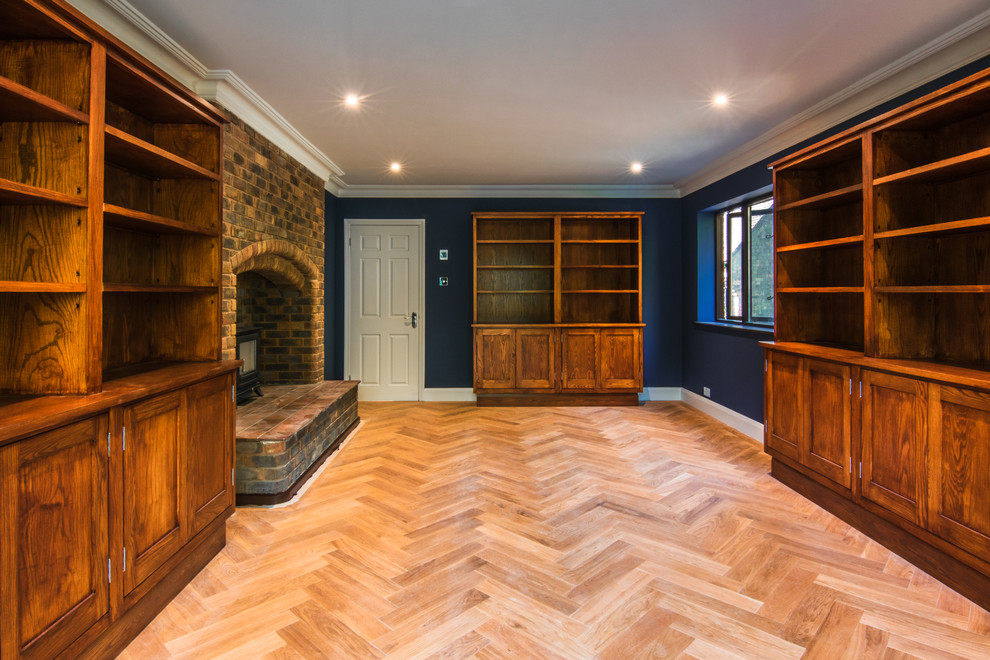 Großes Klassisches Arbeitszimmer mit Arbeitsplatz, blauer Wandfarbe, hellem Holzboden, Kaminofen, Kaminumrandung aus Backstein und freistehendem Schreibtisch in Sussex