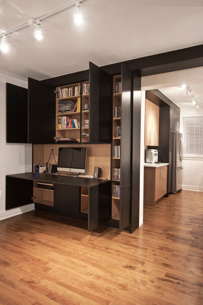 Small contemporary home studio in Montreal with black walls, medium hardwood flooring, no fireplace and a built-in desk.