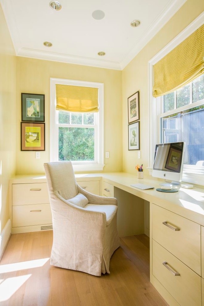 Klassisk inredning av ett hemmabibliotek, med gula väggar, ljust trägolv och ett inbyggt skrivbord