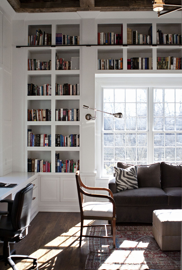 Foto på ett mycket stort lantligt arbetsrum, med ett bibliotek, vita väggar, mörkt trägolv, ett inbyggt skrivbord och brunt golv