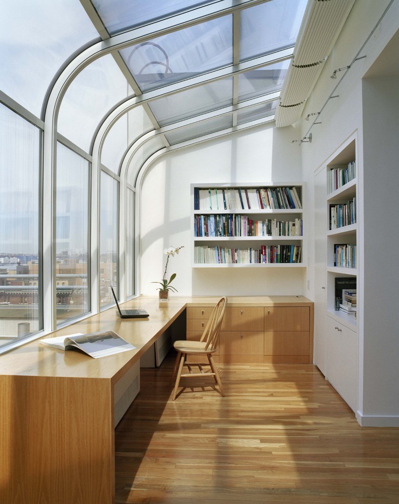 Mittelgroßes Modernes Lesezimmer ohne Kamin mit weißer Wandfarbe, hellem Holzboden, Einbau-Schreibtisch und braunem Boden in New York