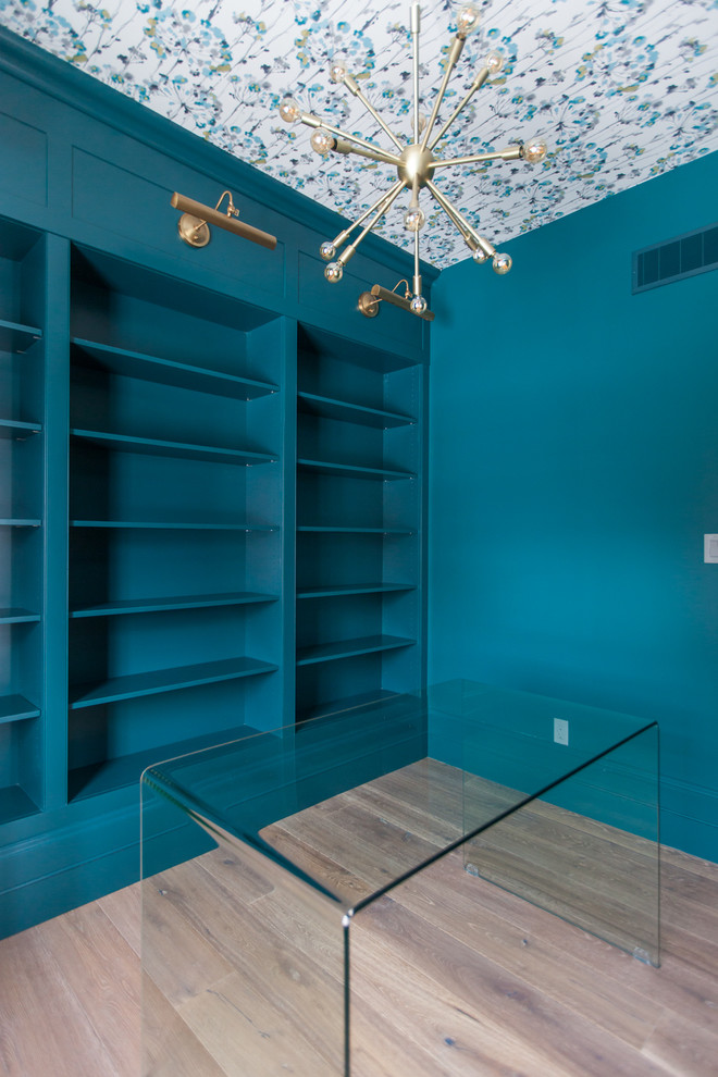 Modelo de despacho actual de tamaño medio con suelo de madera en tonos medios, paredes azules, escritorio independiente y suelo marrón