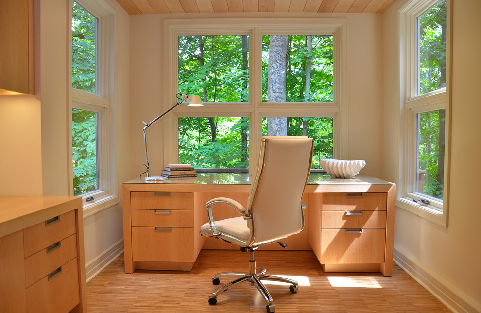 Trendy freestanding desk medium tone wood floor home office photo in Milwaukee with beige walls