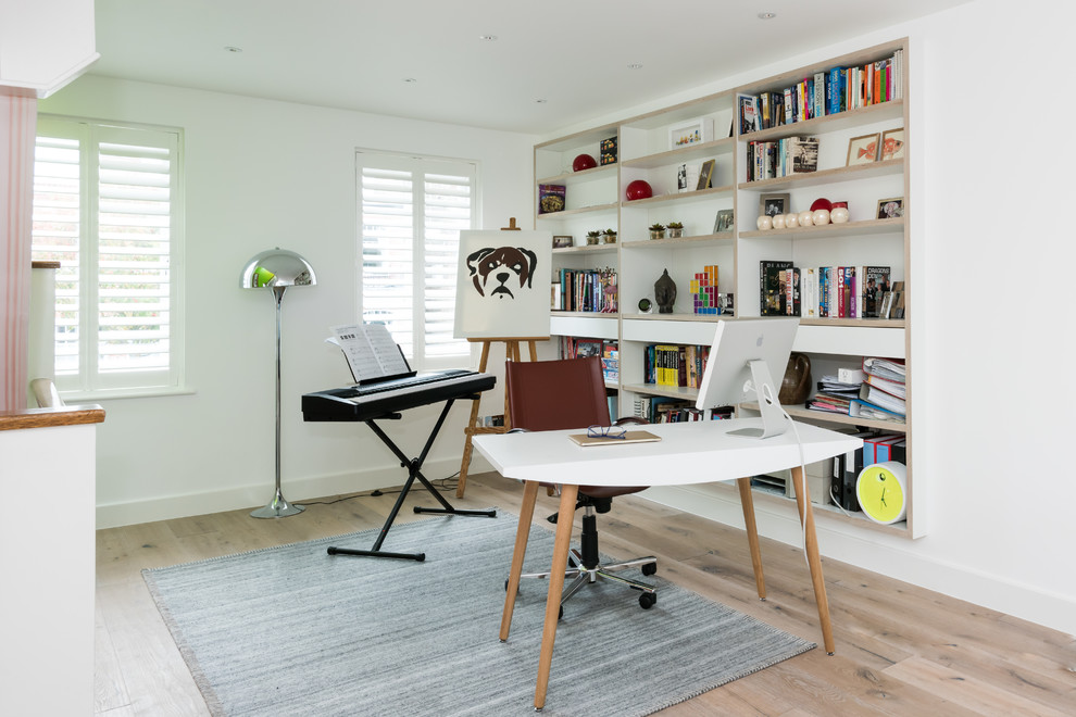 Ejemplo de estudio contemporáneo de tamaño medio con paredes blancas, suelo de madera clara y escritorio independiente