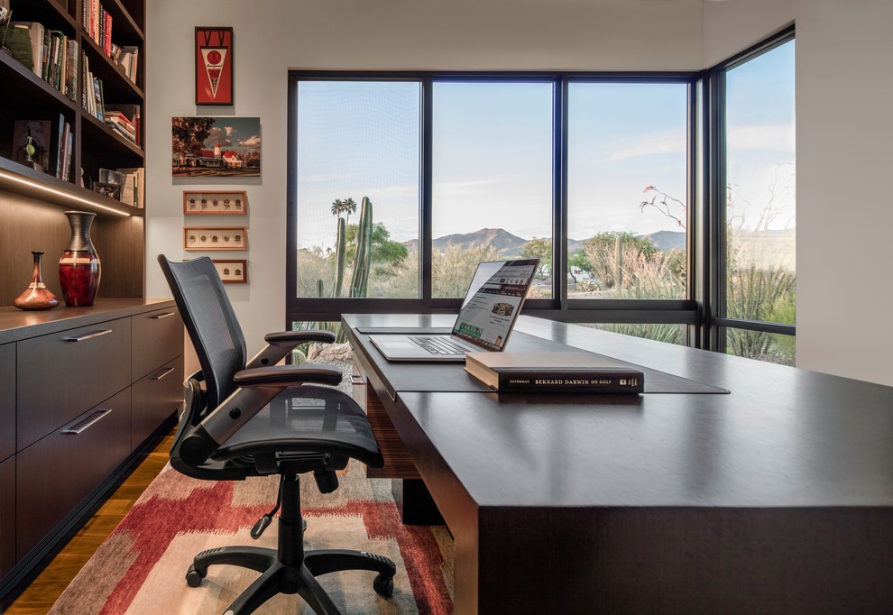 Diseño de despacho actual con paredes blancas, suelo de madera en tonos medios, escritorio independiente y suelo marrón