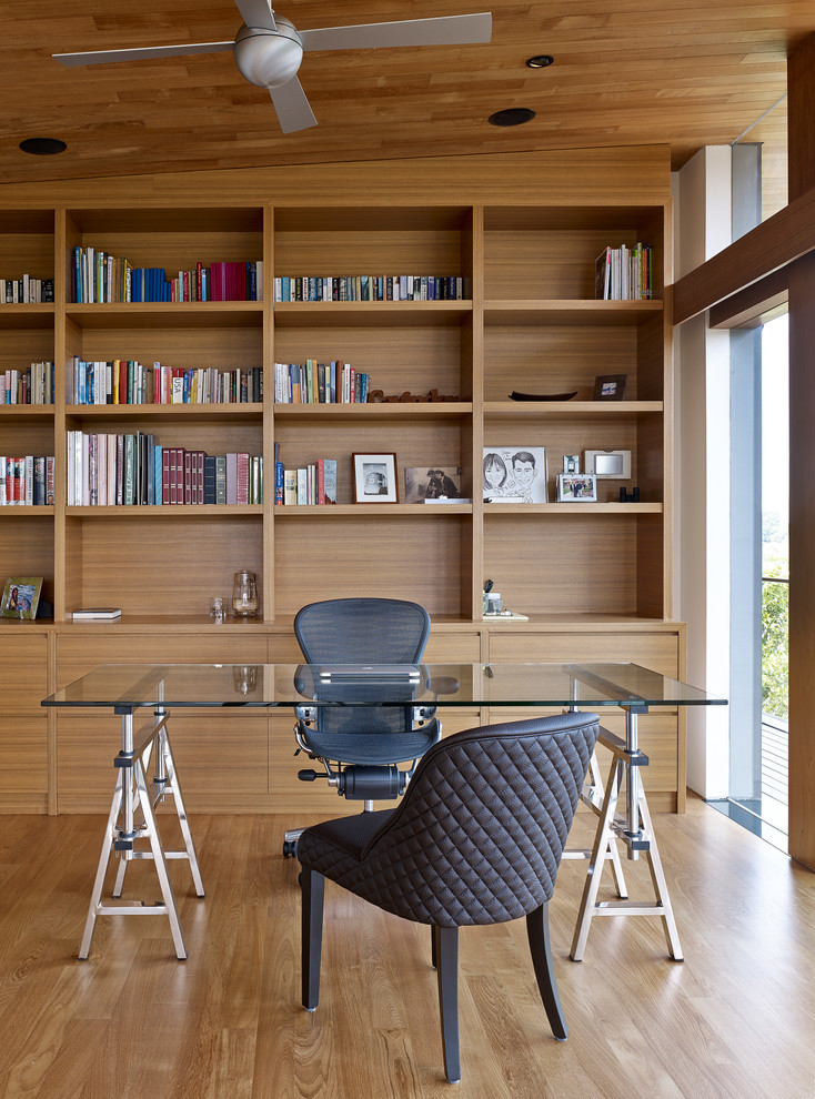 Inredning av ett modernt hemmabibliotek, med bruna väggar, ljust trägolv och ett fristående skrivbord