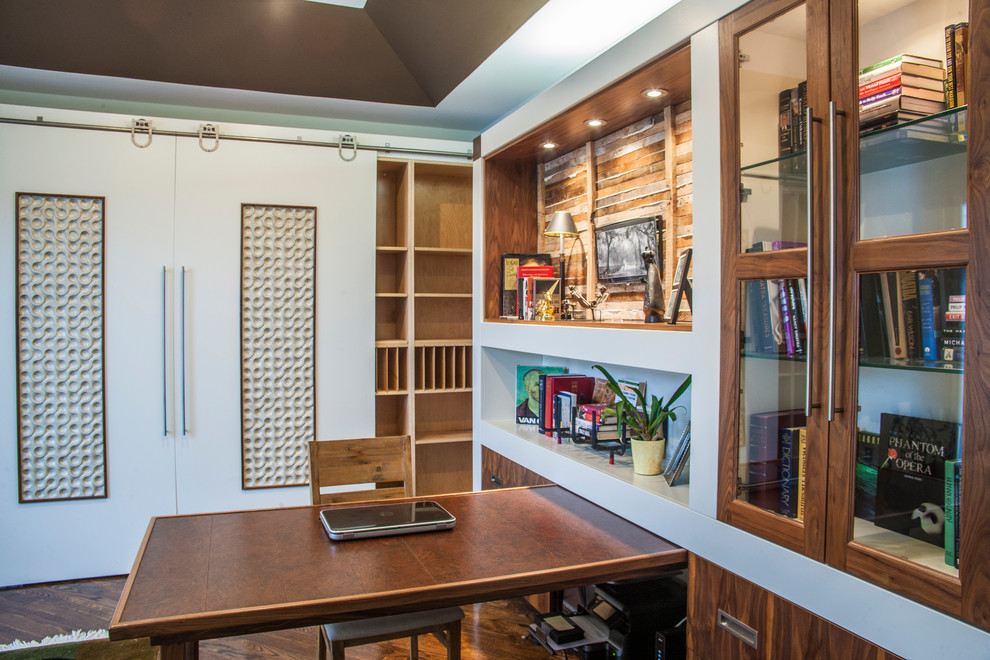 Medium sized contemporary study in Detroit with beige walls, a built-in desk and brown floors.