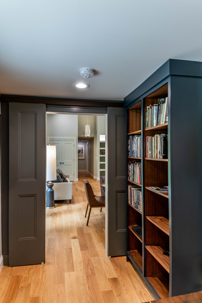 Foto på ett mellanstort funkis arbetsrum, med ett bibliotek, grå väggar, ljust trägolv, en öppen vedspis, en spiselkrans i metall, ett fristående skrivbord och brunt golv