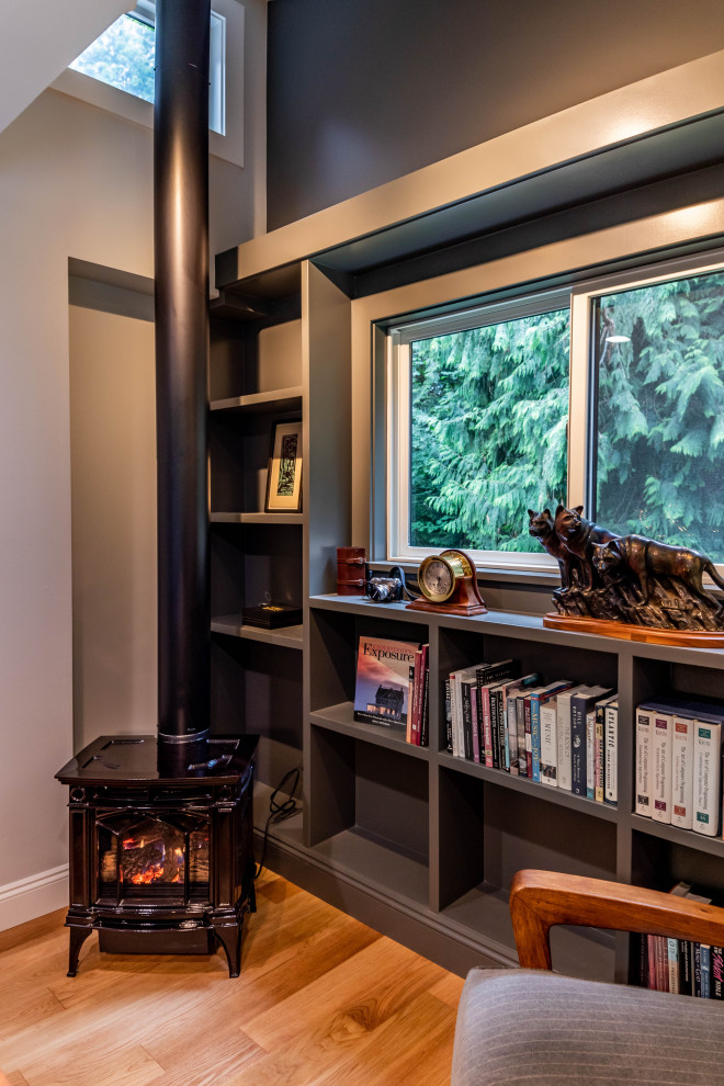シアトルにある高級な中くらいなコンテンポラリースタイルのおしゃれなホームオフィス・書斎 (ライブラリー、グレーの壁、淡色無垢フローリング、薪ストーブ、金属の暖炉まわり、自立型机、茶色い床) の写真